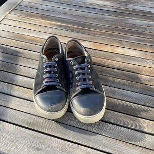 Svarta sneakers från Lanvin i skinn - Snygga svarta sneakers från Lanvin med ovandel i mocka och skinn, rund tå och vita gummisulor. Skorna har blivit slitna på cap toen och snörena är missfärgade men går att hitta nya billigt.!!! ingen box eller dustbag medföljdes!!!