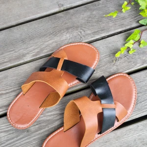 Bruna och svarta sandaler i skinn - Snygga sandaler i storlek 38 med bruna och svarta remmar i skinn. Platt sula och öppen tå, perfekt för varma dagar. Stilren design med kontrasterande färger som passar till många outfits.