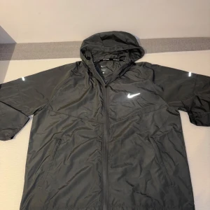 Nike Miler Jacka – Grå - Säljer min grå Nike-jacka. Använd bara ett fåtal gånger, ser helt ny ut. Snygg passform och skön att ha på sig. Perfekt nu till hösten! Passa på innan den försvinner!