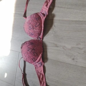 Rosa spets-bh med blommigt mönster - Säljer en snygg rosa Push up bh med blommigt spetsmönster och vadderade kupor. Axelbanden är justerbara och framtill finns en liten rosett. Perfekt för dig som gillar romantiska detaljer och vill ha något extra fint under kläderna.