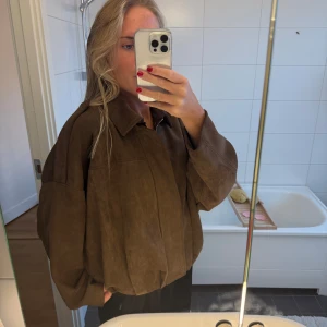 Brun oversized mockajacka - Säljer en brun oversized mockajacka med breda ärmar och klassisk krage. Jackan har dragkedja framtill och en loose passform som ger en chill vibe. Perfekt för dig som gillar en avslappnad men ändå snygg stil.