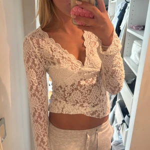 Vit spetsblus med v-ringning - Superfin vit blus i spets med v-ringad hals och långa ärmar. Blusen är genombruten med blommigt spetsmönster och har en feminin, figurnära passform. Perfekt för dig som vill ha en romantisk och trendig look.