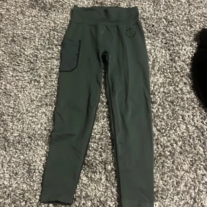 Mörkgröna leggings från MM Sports - Mörkgröna leggings från MM Sports med hög midja och praktisk ficka på sidan. Tight passform och stretchigt material som passar perfekt för träning. Diskret logga framtill och mjuk känsla mot huden. Ordenarie pris 500