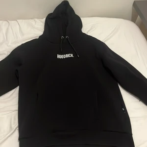 Svart hoodie från Hoodrich strl L - Svart hoodie från Hoodrich i storlek Large med vit logga på bröstet. Klassisk modell med huva och snörning, samt långa ärmar. Perfekt för en chill och stilren streetwear-look.