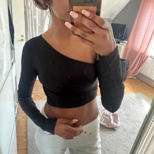 Svart one shoulder topp   - Svart croppad topp  med lång ärm på ena sidan och offshoulder på andra. Tight passform och ribbad struktur. Aldrig använd! 