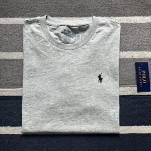 Grå t-shirt från Polo Ralph Lauren - Snygg grå t-shirt från Polo Ralph Lauren med klassisk rund hals och broderad logga på bröstet. Modellen är slim fit och tillverkad i mjuk bomull som känns skön mot huden. Perfekt för en clean och stilren look.