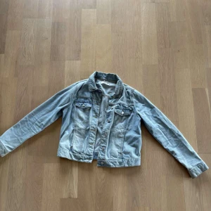 Ljusblå jeansjacka från Mango - Snygg ljusblå jeansjacka från Mango med klassisk krage, bröstfickor med knappar och raka sömmar. Jackan har långa ärmar och silverfärgade knappar framtill. Perfekt för dig som vill ha en tidlös denimlook.