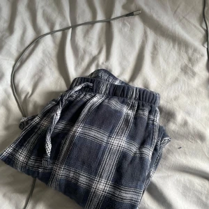 Rutiga mjukisbyxor med snörning - Mysiga mjukisbyxor i mörkblått och vitt rutigt mönster. Byxorna har resår i midjan och snörning för extra komfort. Perfekta för chill dagar hemma eller när du vill vara extra bekväm.