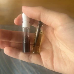 Parfymprover Kayali & Essence - Två parfymprover: Kayali Vanilla 28 i en liten genomskinlig sprayflaska med vit kork och mörk vätska, samt Essence Carashmellow i ett litet glasrör med ljusgul vätska. Perfekt för dig som vill testa nya dofter i smidigt format.