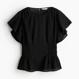 Svart blus med volangärm - Svart blus med breda, luftiga volangärmar och smockdetaljer i midjan som ger en snygg siluett. Blusen har rund halsringning och lätt utsvängd nederkant. Perfekt för dig som gillar en stilren men ändå lekfull look.