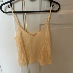 Beige linnetopp från Vanessa Bruno - Supersöt beige/ljusgul linnetopp från Vanessa Bruno med tunna justerbara axelband och v-ringning. Luftig och lätt i materialet, perfekt för varma dagar eller lager på lager. Enkel och stilren design som är lätt att matcha med olika outfits.