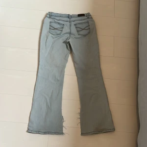Ljusblå bootcut jeans John Baner - Snygga ljusblå bootcut jeans från John Baner med klassiska fem fickor och coola detaljer på bakfickorna. Jeansen har låg midja och är tillverkade i mjukt denimtyg. Perfekta för en avslappnad och trendig look.