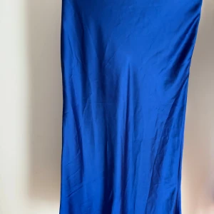 Kornblå kjol i satin från Lindex - Snygg kjol i kornblå satin med slät yta och diskret glans. Kjolen stängs på sidan med en dragkedja. Tyvärr har jag råka riva upp en söm på framsidan, samt att det finns en fläck. Detta är inte så synligt om man inte vet om det. Fläcken går säkert att få bort om man har ett bra knep! 