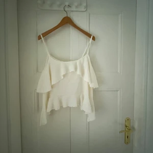 Vit volangtopp från Nelly - Supersöt vit topp från Nelly med tunna axelband och volangdetaljer både framtill och nedtill. Perfekt för varma dagar när du vill ha en luftig och trendig look. Toppens material känns lätt och flowy, och den är enkel att matcha med jeans eller kjol.