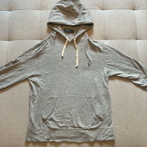 Grå hoodie från Polo Ralph Lauren - Snygg grå hoodie från Polo Ralph Lauren med klassisk broderad logga på bröstet. Priset är ej hugget i sten och tveka inte för att skriva vid funderingar/frågor!