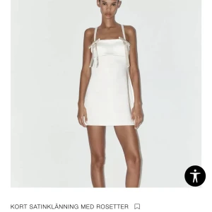 Vit satinklänning med rosetter - Superfin kort klänning i vit satin med smala axelband och söta rosetter framtill. Slutsåld på Zara, säljer pga för liten. Aldrig använd och prislappen finns kvar. Pris kan diskuteras vid snabb affär🌟