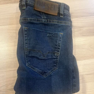 Mörkblå Diesel Ducati jeans - Snygga mörkblå jeans från Diesel med Ducati-detalj på bakfickan. Klassisk femficksmodell med raka ben och normal passform. Jeansen har läderpatch med Diesel-logga i midjan och är tillverkade i slitstarkt denimtyg.  OBS!!! Kan vara lite tighta då de har krympt i tvätten lite 