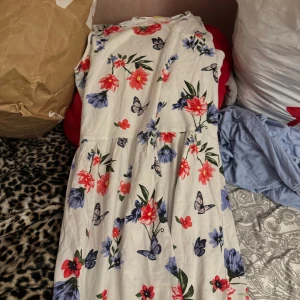 Vit blommig klänning från H&M - Superfin vit klänning från H&M med färgglada blommor i rött, blått och lila samt fjärilar. Klänningen är ärmlös, har rund hals och ett flowy fall. Perfekt för sommarens alla tillfällen och riktigt söt på!