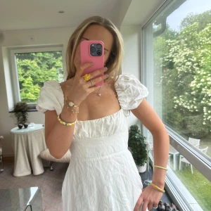 Vit kort klänning med puffärmar - Superfin vit kort klänning med puffärmar och fyrkantig urringning. Öppen rygg med snörning som ger en snygg detalj. Klänningen har en lätt A-linjeform och är gjord i ett tunt, somrigt tyg. Perfekt för varma dagar och ger en romantisk vibe.