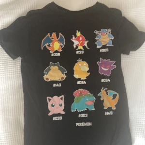 Svart Pokémon t-shirt med tryck - Svart t-shirt från Pokémon med färgglatt tryck av nio klassiska Pokémon-figurer på framsidan. Modellen är kortärmad och har rund hals. Perfekt för dig som älskar Pokémon och vill sticka ut med en cool och lekfull stil.