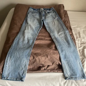Ljusblå raka jeans - Säljer ett par klassiska ljusblå jeans med rak passform. Jeansen har fem fickor, normal midja och är tillverkade i bomull. Perfekta för en avslappnad och tidlös look.