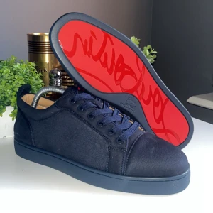 Mörkblå sneakers från Louboutin - Snygga mörkblå sneakers från Louboutin i mocka med klassisk röd sula och broderad logga på hälen. Skorna har rund tå, platt sula och matchande mörkblå snörning. Perfekta för dig som vill sticka ut med exklusiv streetstyle.