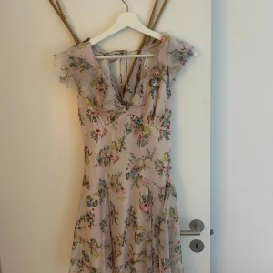 Blommig kortklänning från ASOS Design - Supersöt kortklänning från ASOS Design i ljus, nästan champagnefärgad ton med blommigt mönster i pastell. Klänningen har v-ringning, volangdetaljer vid ärmarna och är tillverkad i ett tunt, luftigt material. Perfekt för sommarens alla tillfällen! Använd max 3 gånger.