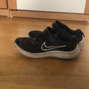 Nike Star Runner svarta sneakers - Svarta Nike Star Runner sneakers med vit sula och klassisk swoosh på sidan. Ovandel i mesh och syntet för bra andningsförmåga, snörning och kardborreband för enkel påtagning. Perfekta för dig som gillar sportig stil och vill ha bekväma skor till vardags.