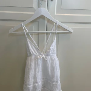 Vit sommarklänning från Gina Tricot - Supersöt vit topp från Gina Tricot med tunna axelband, v-ringning och knyt bak. perfekt för varma dagar. Enkel och fräsch stil som passar till sommaren. Aldrig använt 
