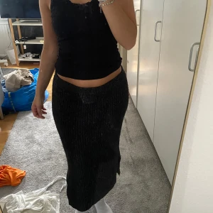 Svart ribbad stickad långkjol - Säljer en svart ribbad stickad långkjol med slits på sidan. Kjolen är mjuk och följsam, perfekt för dig som gillar en chill och snygg look. Den har en rak passform och är superenkel att matcha med både crop tops och hoodies.