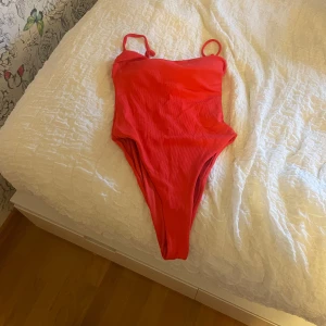 Röd baddräkt med smala axelband - Snygg röd baddräkt med smala axelband som är avtagbara samt högt skurna ben. Enkel och stilren design som passar perfekt för stranden eller poolen. Materialet känns mjukt och följsamt mot huden. 