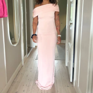 Meshki Ljusrosa offshoulder långklänning - Elegant ljusrosa långklänning med offshoulder-design och figurnära passform. Klänningen har en mjuk, stretchig känsla och sveper snyggt längs kroppen. Perfekt för dig som vill ha en stilren och romantisk look.