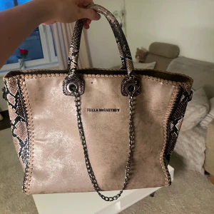 Stella McCartney Python Falabella Tote Bag - Väska från Stella McCartney i beige med ormmönstrade detaljer på handtag och sidor, köpt på secondhandbutik och ses som en Vinted väska från Stella McCartney. Däremot som man kan se så har väskan tappat ett S på framsidan, och extra axelbandet som man får med är även sönder på ena klippan som man kan se på fjärde- bilden. Men förutom de två skadorna är väskan i utmärkt skick!