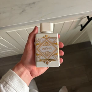 Badee Al Oud Honor & Glory parfym - Parfymen Badee Al Oud Honor & Glory från Lattafa kommer i en vit, fyrkantig flaska med guldiga orientaliska mönster och detaljer. Flaskan rymmer 100 ml och har en lyxig känsla med sin eleganta design och guldfärgade etikett undertill.
