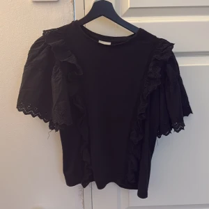 Svart blus med volang från Sofie Schnoor - Supersnygg svart blus från Sofie Schnoor med korta puffärmar och broderade volangdetaljer.