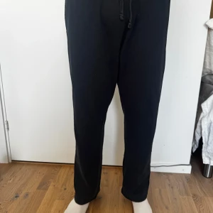 Svarta mjukisbyxor med snörning - Svarta mjukisbyxor med elastisk midja och snörning. Byxorna har raka ben och sidofickor, perfekta för chill dagar eller träning. Tillverkade i mjukt bomullsmaterial för maximal komfort.