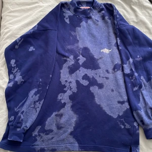 Blå oversized sweatshirt New Wave - Säljer en blå oversized sweatshirt från New Wave med unikt blekt mönster och broderad logga på bröstet. Tröjan har lång ärm, hög krage och är gjord i mjuk bomull. Perfekt för dig som gillar streetwear och vill sticka ut med en cool look.