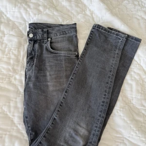 Grå jeans från J.Lindeberg, 30/32 - Snygga grå jeans från J.Lindeberg i klassisk femficksmodell. Jeansen har en rak passform och är tillverkade i mjukt denimtyg med diskret tvättad look. Silverfärgade detaljer och logoknapp framtill. Perfekta för en stilren vardagsoutfit.