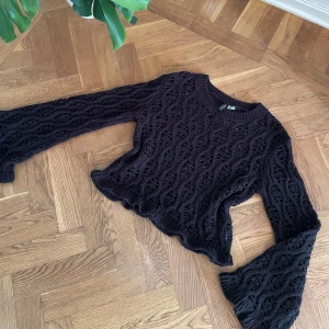 Svart stickad tröja med utsvängda ärmar - Supersnygg svart stickad tröja  med vågigt hålmönster och utsvängda långa ärmar. Croppad modell med ribbade kanter och unik struktur som ger en cool och trendig vibe. Perfekt att styla med jeans eller kjol.