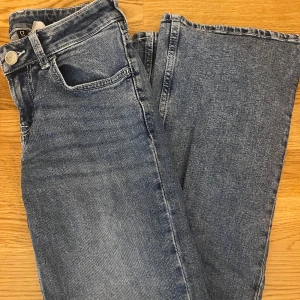 Blå raka jeans från Divided H&M - Säljer ett par blå jeans från Divided H&M i storlek 32. Utsvängda med fem fickor och låg i midjan. Tillverkade i bomull med snygg tvättad look och ljusare partier på låren. 