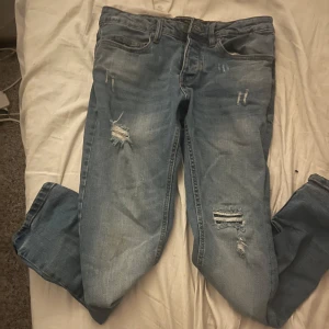 Ljusblå slitna jeans W29 L30 - Ljusblå jeans från Sons med snygga slitningar och trasiga detaljer på benen. Klassisk femficksmodell med normal passform och raka ben. Jeansen har en fräsch tvätt och är perfekta för en avslappnad streetstil. Priset kan diskuteras 