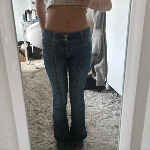Blå bootcut jeans med dubbla knappar - Snygga blå jeans med bootcut-modell och låg midja. Jeansen har dubbla knappar i midjan, klassiska fickor och markerade sömmar framtill. Materialet är jeans med en lätt stretch och tvättad look. Jag är 157-158 och bär strl 32. Skriv angående frågor eller fler bilder🫶🏽