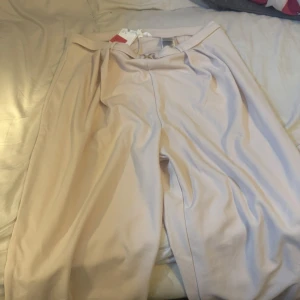 Beige vida kostymbyxor med bälte - Stilrena beige kostymbyxor från  Hm  med vida ben och snyggt bältedetalj framtill i silver. Byxorna har hög midja och är perfekta för en clean och trendig look. Sköna och lätta att matcha med både sneakers och boots. Den är inte använd prislapp kvar .