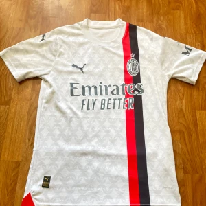 AC Milan vit bortatröja Puma - AC Milan bortatröja i vitt med subtilt mönster, svarta och röda vertikala ränder på framsidan. Puma-logga på bröstet, klubbmärke och sponsortryck. Tillverkad i lätt och ventilerande polyester med korta ärmar. 200kr är sista pris!