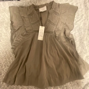 Grön volangblus från Neo Noir - Supersöt blus i smoke green från Neo Noir med volangdetaljer och broderade partier. Luftig och lätt, med v-ringning och ärmlös design. Perfekt för dig som gillar Stockholm stil. Modellen heter Jayla S Voile Top. Prislappen är kvar helt oanvänd säljer pga att jag redan har en i vit. Nypris: 599 kr från Åhléns, storlek 36 men funkar även ifall man har storlek 34 och 38!