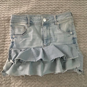 Ljusblå jeanskjol med volang Page One - Superfin ljusblå jeanskjol från Page One Young i high waist-modell. Kjolen har volang nertill och råa kanter för en cool look. Klassiska fickor fram och bak, perfekt till sneakers eller boots. Priset går alltid att dusketera 