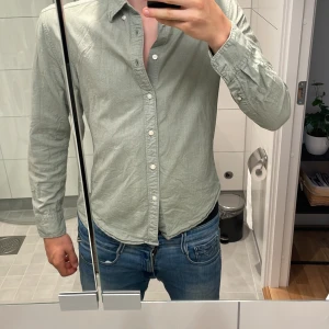 Ljusgrön skjorta från East West - Säljer en stilren ljusgrön skjorta från East West i slim fit-modell. Skjortan har klassisk krage, långa ärmar och knäppning framtill med vita knappar. Perfekt för dig som gillar en enkel och fräsch look.