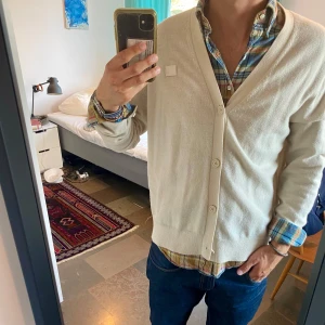 Beige kofta från Acne Studios - Snygg beige kofta från Acne Studios i klassisk modell med v-ringning och knappar framtill. Tillverkad i mjukt material som känns lyxigt och passar perfekt till lager-på-lager. Enkel att styla med skjorta eller t-shirt för en clean look.