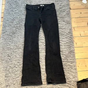Svarta bootcut jeans med fickdetaljer - Snygga svarta jeans med bootcut passform och klassiska fem fickor. Baktill finns fickor med lock och knappdetaljer. Jeansen har normal midja och är tillverkade i ett mjukt bomullsmaterial med lite stretch för extra komfort.