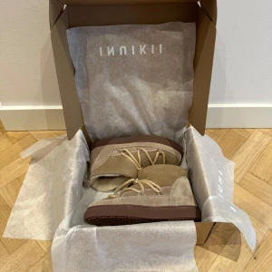 Beige mockaboots från Inuikii - Snygga beige skor från Inuikii i mocka. Skorna är aldrig använda pga köpta i fel storlek. De är köpta för 3100kr.  